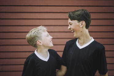Zwei fröhliche Jungen betrachten sich gegenseitig an einer braunen Wand - MASF39638