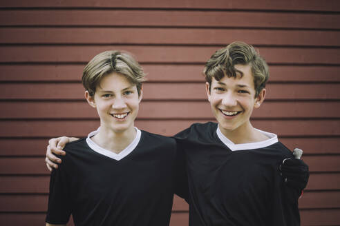 Portrait of happy teenage boys standing with arms around against wall - MASF39640