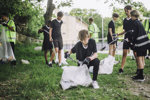 Jugendlicher sammelt Müll in Plastiktüte, umgeben von Freunden in der Nähe - MASF39645