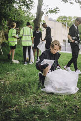 Volunteer kneeling by garbage bag collecting plastic - MASF39646