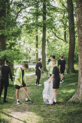 Full length of male friends collecting plastic in garbage bag - MASF39653