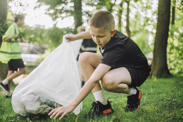 Junge sammelt Müll in Tüte, während er in Hocke sitzt - ein Beispiel für Umweltbewusstsein und Sauberkeit - MASF39654