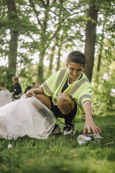 Ein fröhlicher Junge sammelt Müll in einer Tüte auf dem Gras - MASF39657