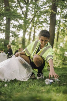 Ein fröhlicher Junge sammelt Müll in einer Tüte auf dem Gras - MASF39657