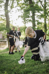 Junger blonder Mann sammelt Plastikmüll in einem Müllsack auf - MASF39661