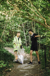 Junge sammeln Müll auf einem Sack inmitten von Pflanzen - MASF39666