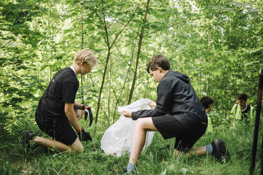 Ein Junge sammelt gemeinsam mit anderen Plastik auf dem Boden auf, während er kniet - MASF39669