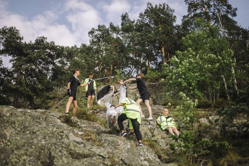 Low angle view of boys collecting garbage from rock formation - MASF39683