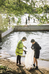 Junge mit Müllsack am Seeufer - ein Zeichen für Umweltbewusstsein und Nachhaltigkeit - MASF39689
