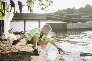 Junge sammelt Plastik am Seeufer auf, um die Umwelt zu schützen - MASF39690