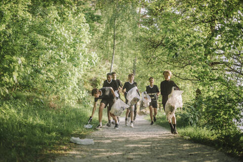 Junge Jogger laufen auf einem grünen Weg umgeben von Bäumen und Natur - MASF39696