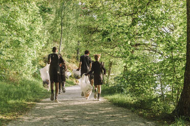 Full length rear view of boys plogging on footpath amidst green plants - MASF39698