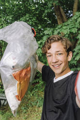 Porträt eines glücklichen Teenagers, der einen Müllsack mit Plastik zeigt - MASF39701