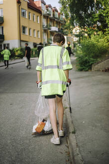 Rückansicht eines Teenagers mit reflektierender Kleidung, der auf der Straße mit einem Müllsack geht - MASF39706