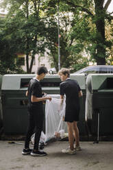 Teenager in voller Länge, der einen Müllsack mit Plastik bei der Recycling-Tonne hält - MASF39716
