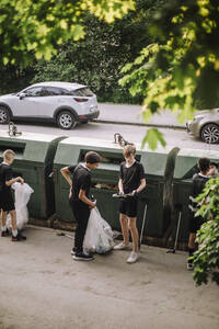 Jungen in voller Länge, die einen Müllsack mit Plastik bei der Recycling-Tonne halten - MASF39717