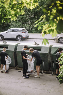 Freiwillige halten in voller Länge einen Müllsack mit Plastik bei der Recycling-Tonne - MASF39718