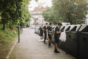 Freunde stehen in voller Länge mit Müllsäcken bei den Recycling-Behältern - MASF39721