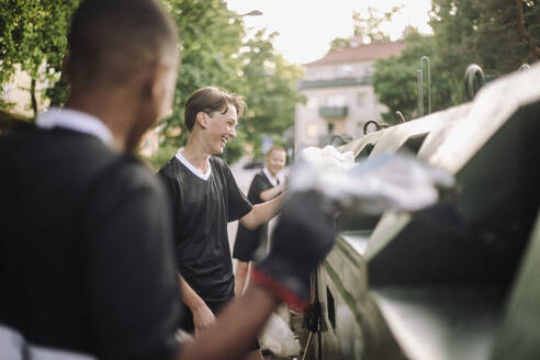 Happy boys putting plastic garbage bags in recycling bins - MASF39727