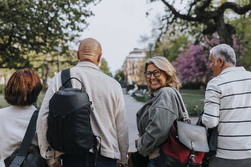 Porträt einer glücklichen älteren Frau, die beim Spaziergang mit Freunden im Park über die Schulter schaut - MASF39740