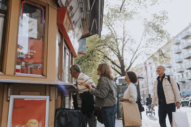 Male and female senior friends buying desert from ice cream shop at street - MASF39745