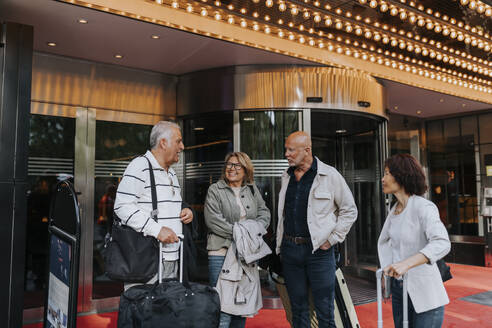 Älterer Mann unterhält sich mit Freunden vor einem Kino, während diese mit Gepäck bereit für die Reise sind - MASF39755