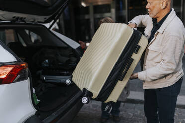 Seitenansicht eines älteren Mannes, der sein Gepäck in den Kofferraum eines Autos lädt - MASF39757
