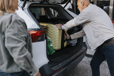 Seitenansicht eines älteren Mannes, der einen Koffer in den Kofferraum eines Autos lädt - MASF39758