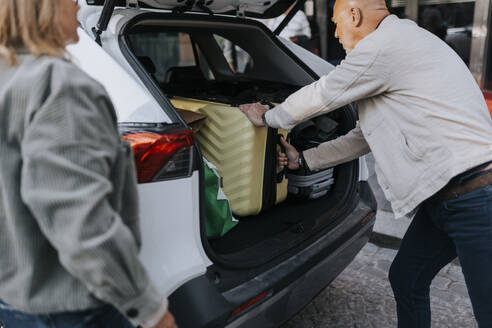 Side view of elderly man loading suitcase in car trunk - MASF39758