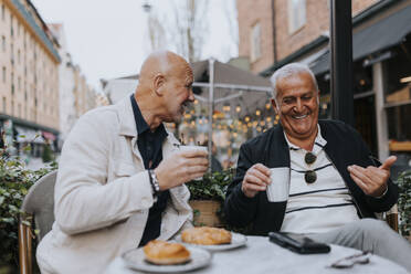 Happy male senior friends enjoying with each other while having coffee at sidewalk cafe - MASF39769