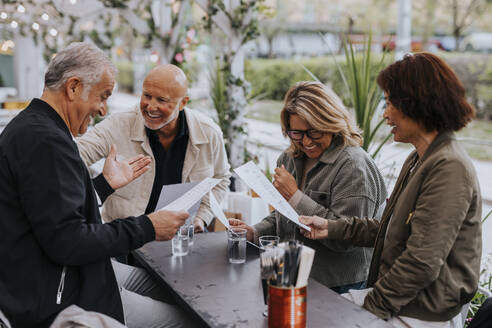 Happy male and female senior friends enjoying while reading menu card at restaurant - MASF39804