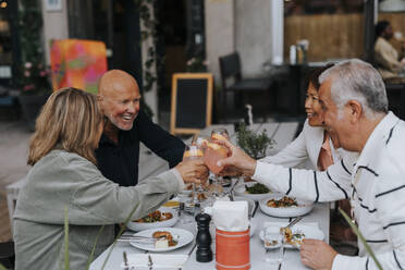 Glückliche männliche und weibliche ältere Freunde stoßen mit Getränken an, während sie im Restaurant essen - MASF39809