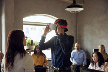 Male and female colleagues watching businessman wearing virtual reality simulator at office - MASF39814