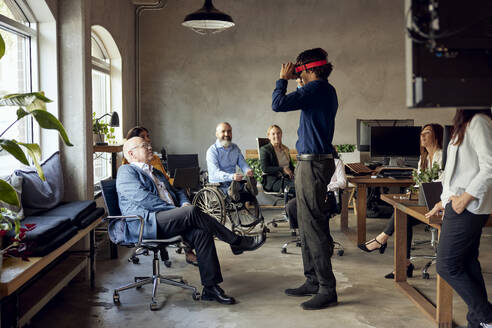 Männliche und weibliche Kollegen beobachten einen Geschäftsmann in einem VR-Simulator im Büro - MASF39817