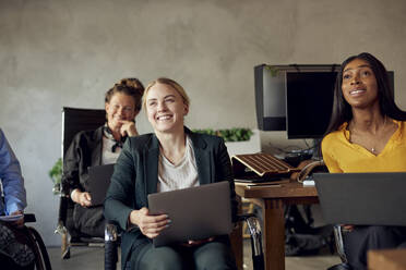 Glückliche weibliche Geschäftskollegen mit Laptops sitzend in einem kreativen Büro während einer Besprechung - MASF39836
