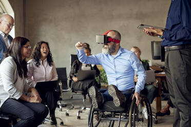 Männliche und weibliche Kollegen betrachten einen Geschäftsmann mit Behinderung, der im Kreativbüro VR schaut - MASF39839
