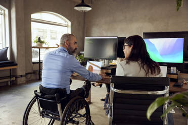 Business colleagues discussing while sitting at desk in office - MASF39842