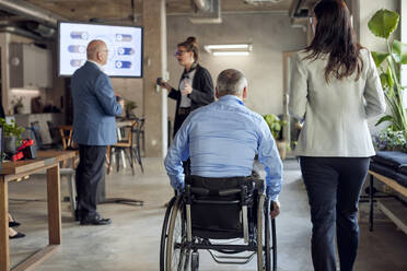 Rückansicht eines Geschäftsmannes mit Behinderung durch eine Geschäftsfrau in der Nähe von Kollegen, die in einem kreativen Büro diskutieren - MASF39853