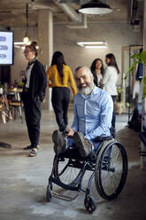 Porträt eines glücklichen Geschäftsmannes mit Behinderung im Rollstuhl im Büro - MASF39865