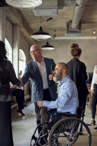 Geschäftsmann und Geschäftsfrau beim Händeschütteln durch einen männlichen Kollegen mit Behinderung im Büro - MASF39871