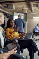 Confident businesswoman gesturing while sitting by female colleague at office - MASF39879