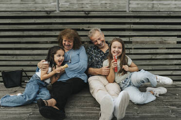 Glückliche Großeltern und Enkelinnen in voller Länge auf der Diele sitzend - MASF39902