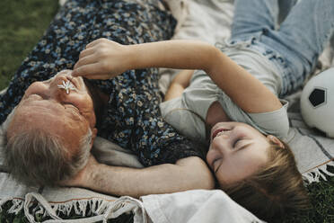 Smiling girl holding flower on grandfather's face while lying together - MASF39906