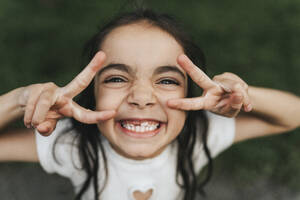 Porträt eines glücklichen Mädchens im Grundschulalter mit Friedenszeichen im Park - MASF39918