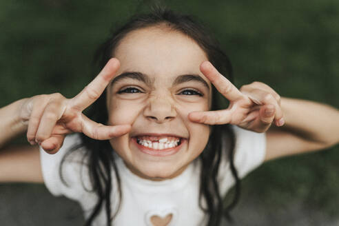 Portrait of happy elementary girl showing peace sign at park - MASF39918