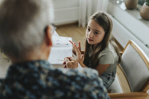 Girl doing homework with grandfather at home - MASF39926