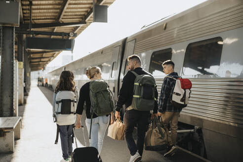 Familie im Gespräch miteinander, während sie mit Gepäck in der Nähe des Zuges am Bahnhof spazieren geht - MASF39933