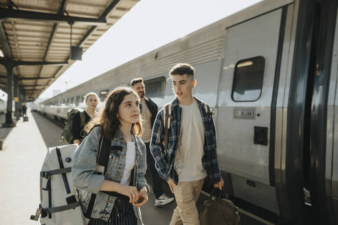 Boy talking to girl carrying luggage while going on vacation - MASF39939