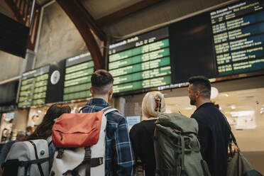 Rückansicht einer Familie mit Rucksäcken, die auf die Ankunft-Abfahrtstafel am Bahnhof schaut - MASF39965