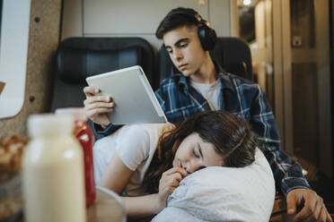 Junge hält Tablet-PC mit Schwester, die im Zug ein Nickerchen macht - MASF39973